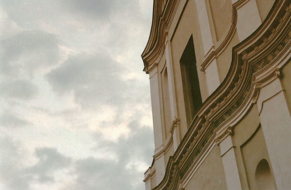 Facciata curva di un edificio con decorazioni architettoniche, vista dal basso contro un cielo nuvoloso.