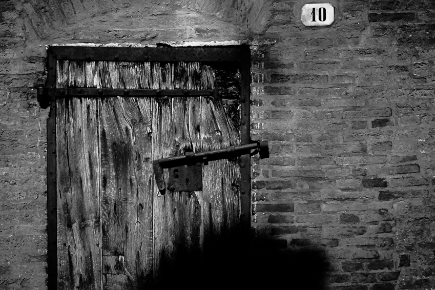 Porta di legno grezzo in un muro di mattoni, con una piccola targa numerata 10 sopra l’ingresso.