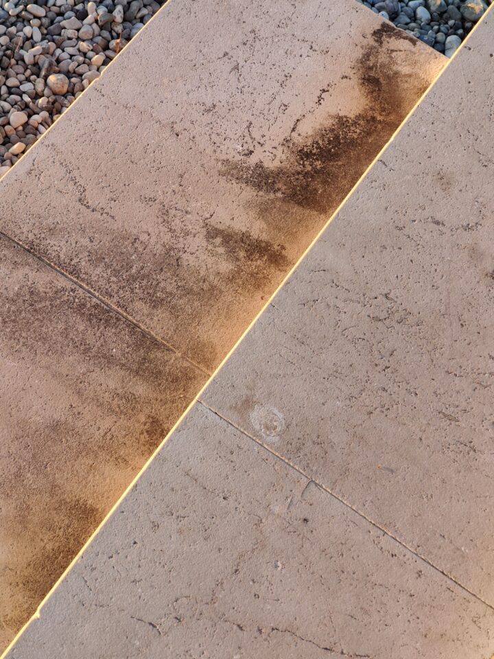 Lastre rettangolari beige accostate, con macchie scure e segni superficiali; sul bordo superiore sinistro si vedono piccoli ciottoli.