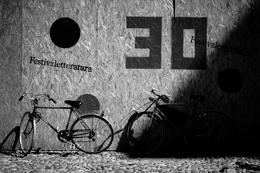 Due biciclette appoggiate a una parete con la scritta “Festivaletteratura” e grandi numeri neri; pavé in primo piano.