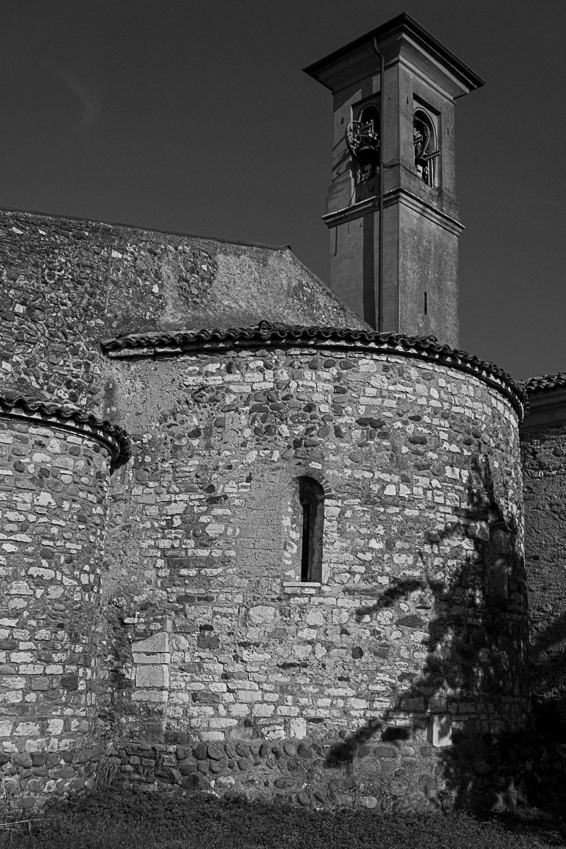 Torre campanaria in pietra sopra una struttura circolare in muratura, con tetti in tegole e una stretta finestra ad arco.